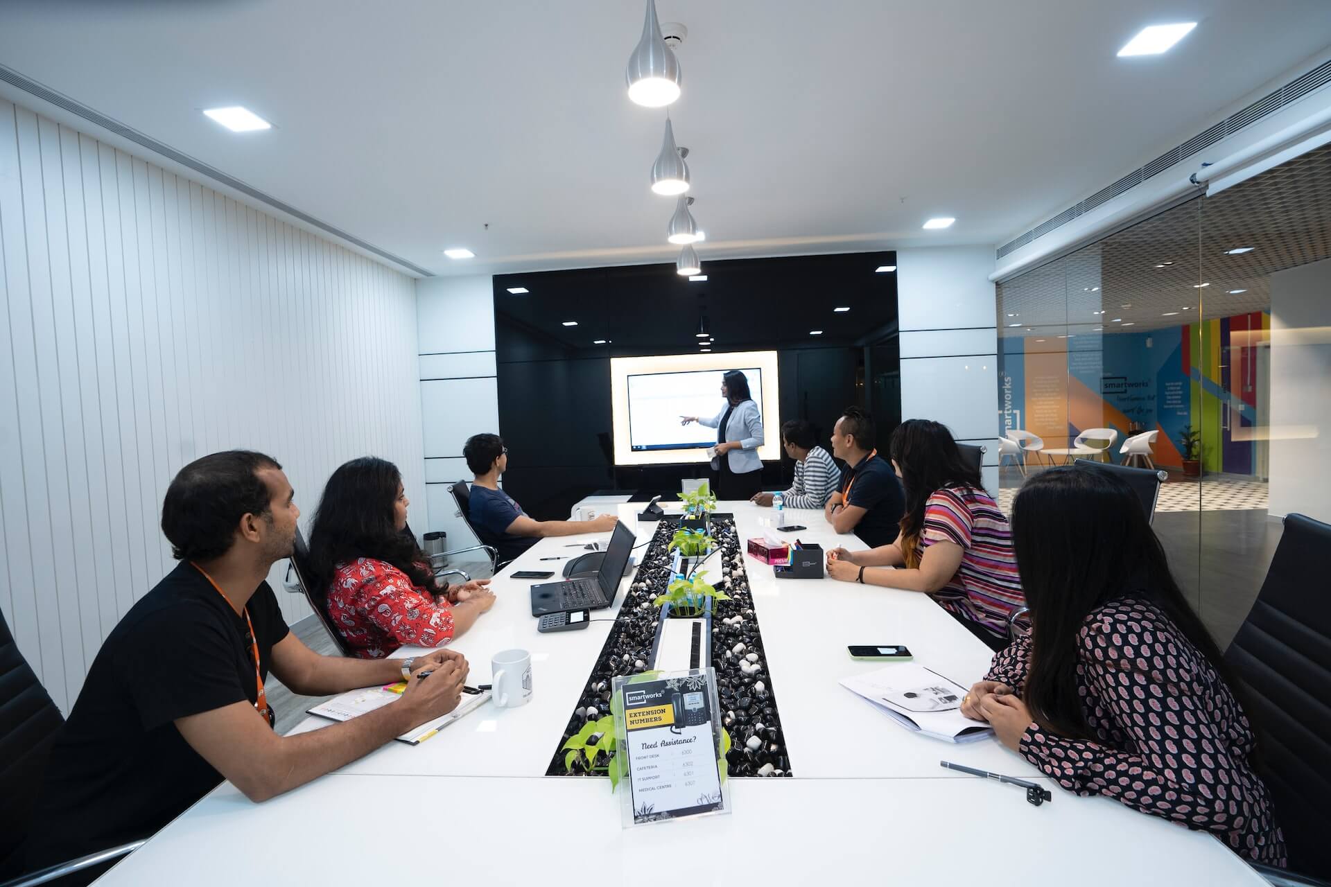 People in a conference room watching a presenter pointing to a screen.